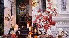 A Halloween wreath on a black front door; pumpkins and spiders on the porch steps.