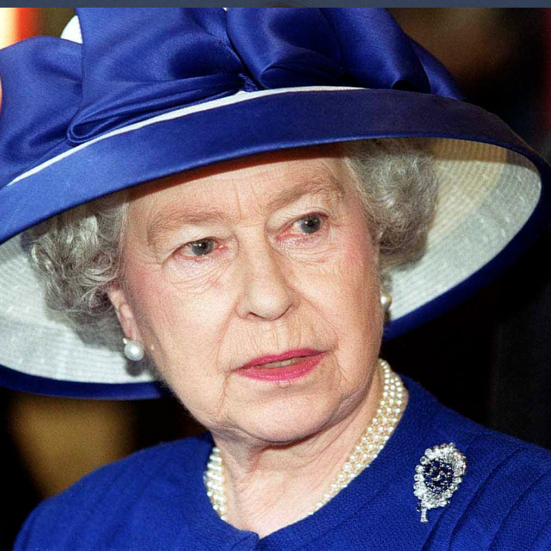 Britain's Queen Elizabeth II during a visit to Fitzalen High School wearing a royal blue suit with a matching wide-brim hat, a pearl necklace, and a sapphire and diamond brooch
