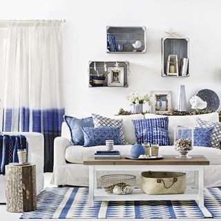 living room with white wall white sofa with designed cushion blue rug and wall pieces