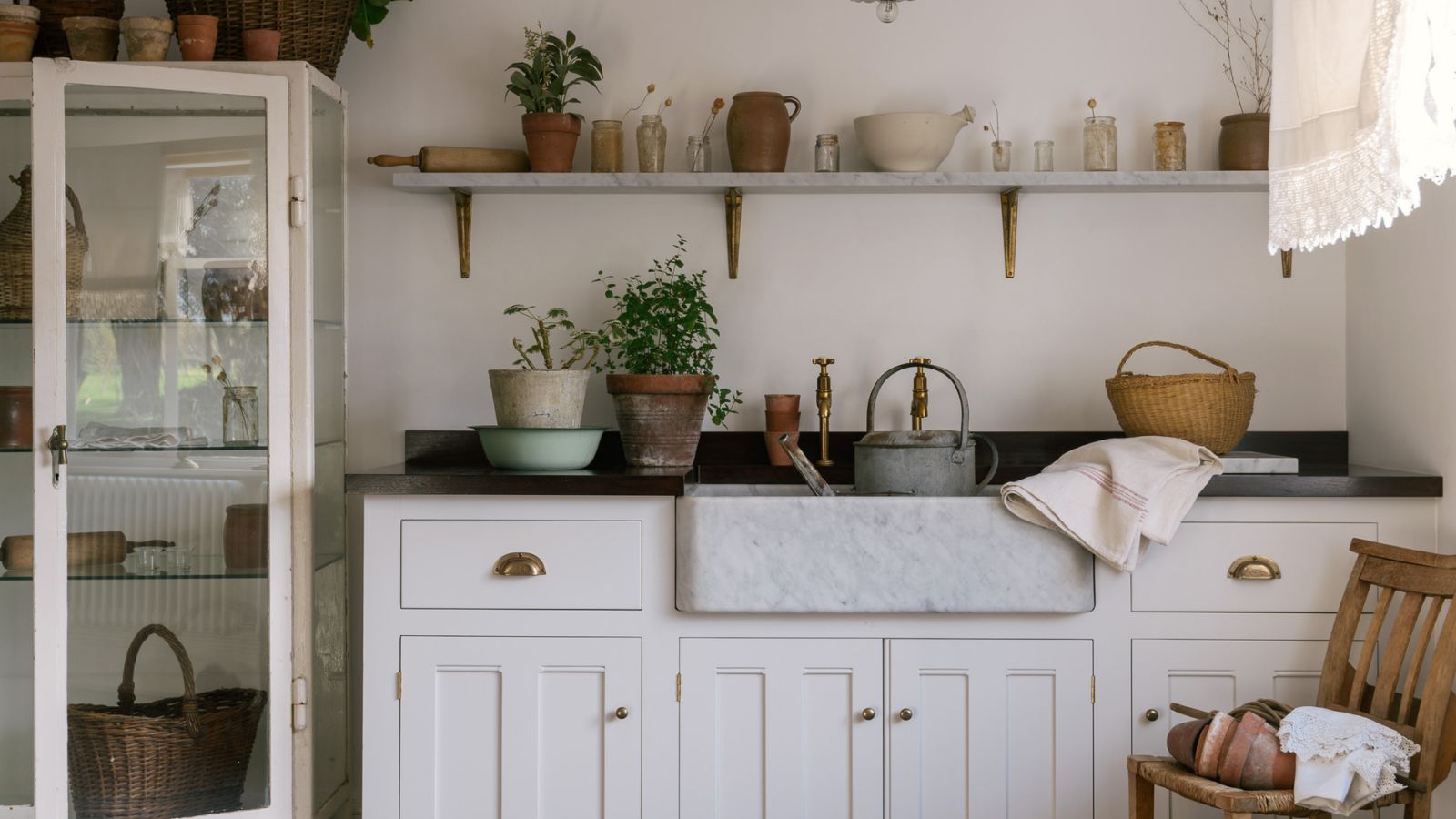 Utility sink area in cottage style home with open shelves and freestanding glass cabinet
