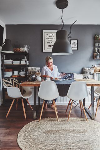 Pendant light ideas: woman sitting at dining table with black wall, dark wood floor, large black statement pendant light over table, and white Eames-style chairs