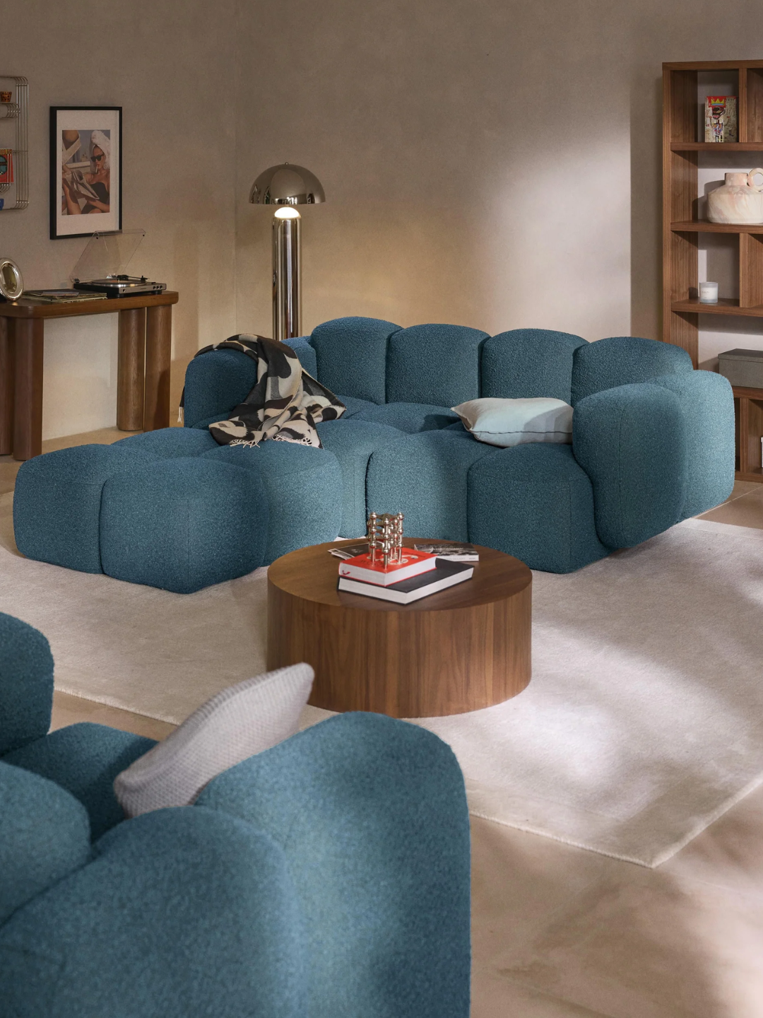A blue boucl&amp;eacute; modular sofa from Westwing in a living room with a chrome floor lamp, and a wood round coffee table