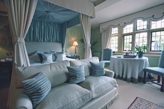 A canopy bed with a blue cover and ornate drapery stands in the middle of a beautiful room at Le Manoir aux Quat'Saisons in England