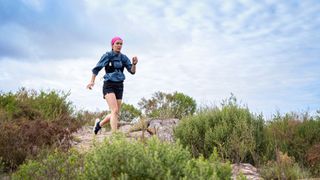 Woman wearing trail vest and headband, running through rocky landscape