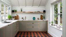 Minimalist kitchen featuring sage green flat-panel cabinets, open wood shelving, and a bold orange and black checkered tile floor.