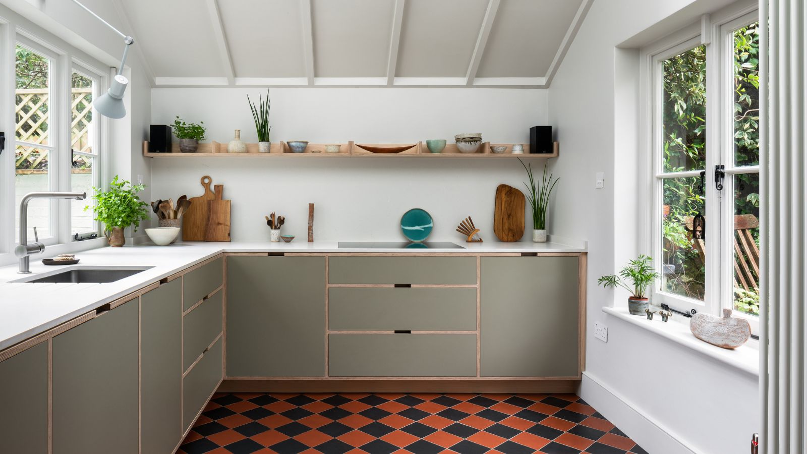 Minimalist kitchen featuring sage green flat-panel cabinets, open wood shelving, and a bold orange and black checkered tile floor.