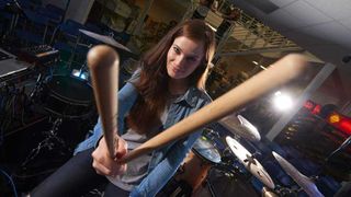 Anika Nilles seated at her drumkit, holding a pair of sticks towards the camera