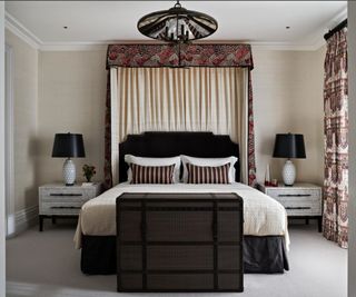 Bedroom with double bed under a canopy with an upholstered headboard, carpeted floor, high ceiling with coving. A seven storey townhouse in Kensington, London, renovated and redesigned in theatrical style, a family home.