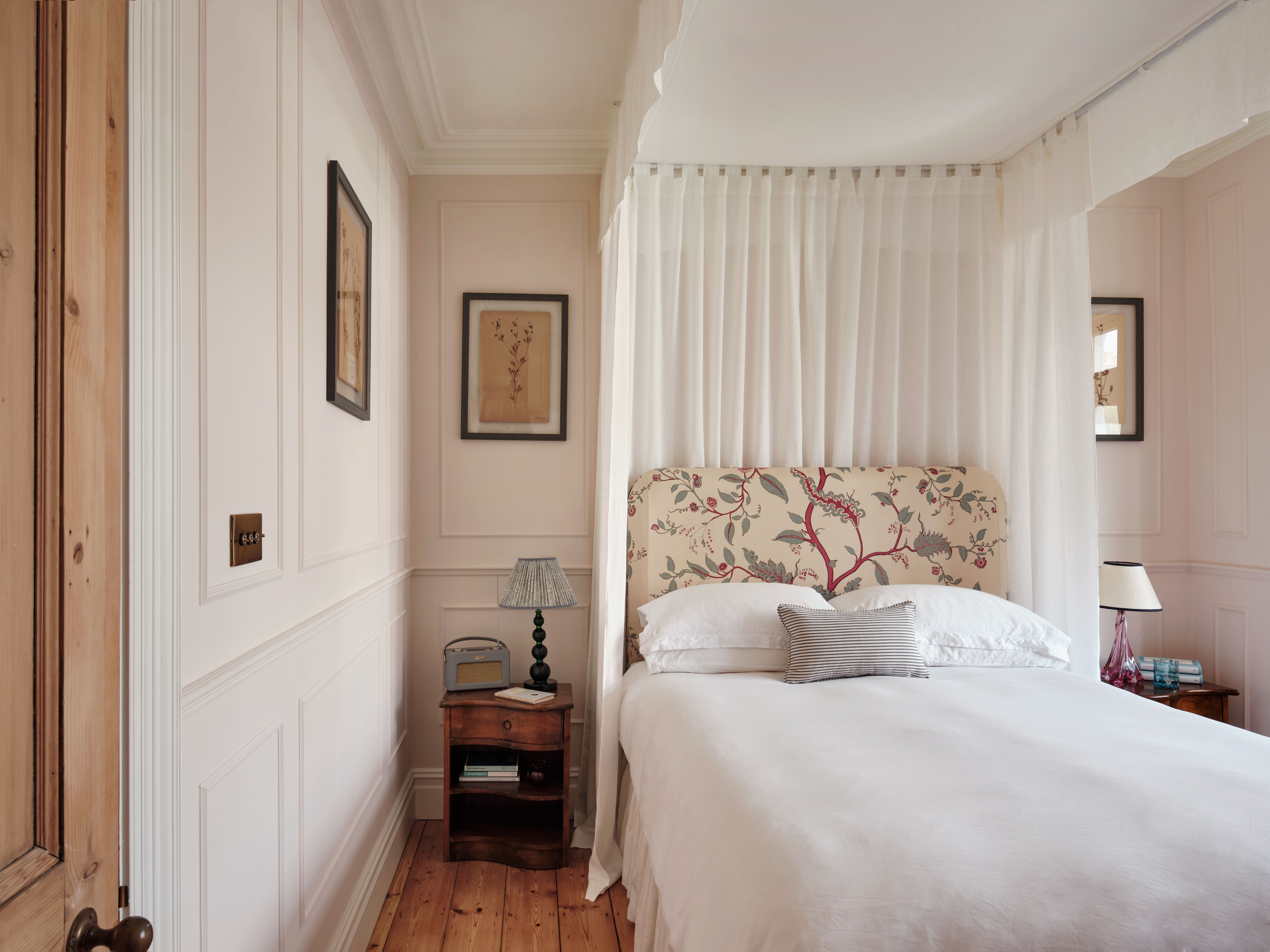Interior shot of a wooden floored home with pale, cream and rose-tinted walls, antique furniture, and statement marble, stone, and wood surfaces, along with curated artwork and textiles.