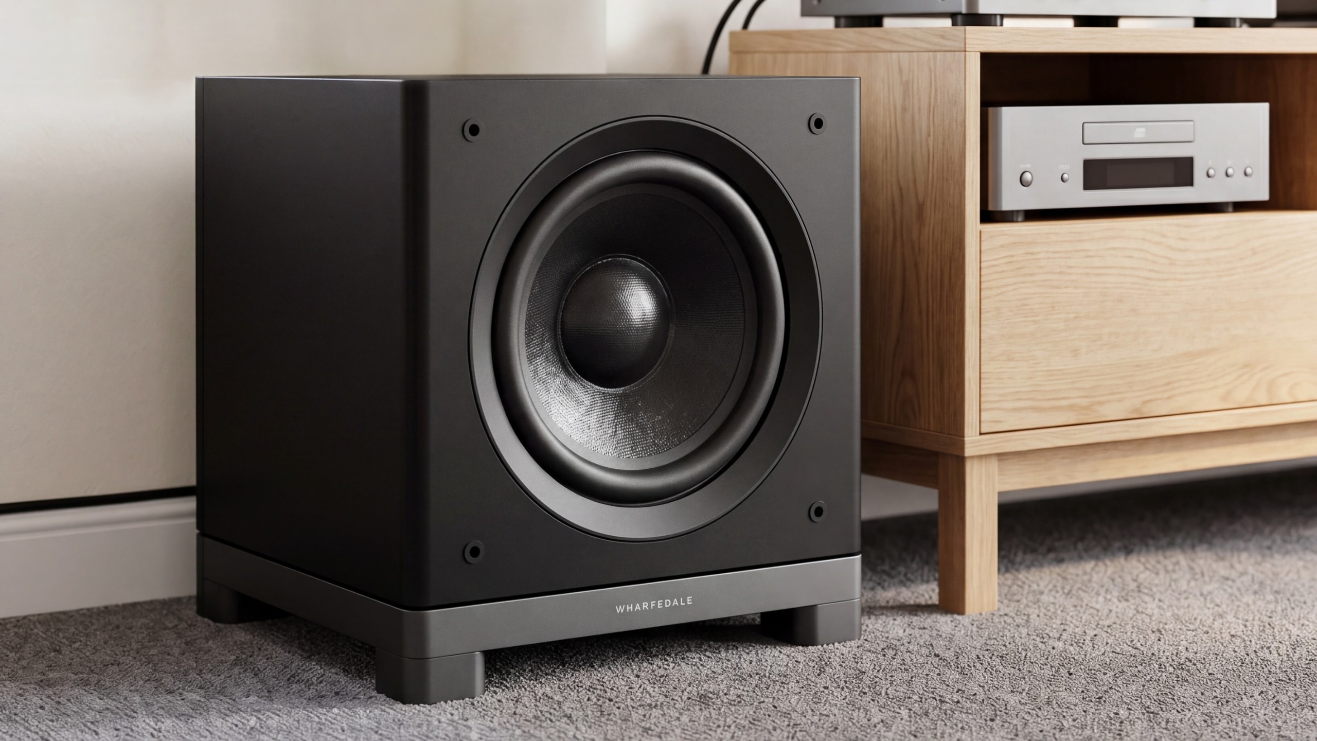 A black Wharfedale Nova 10 subwoofer on a carpet next to a wooden TV stand.
