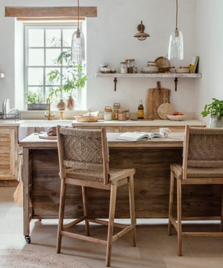 kitchen with natural wood finish units, white walls, mobile wooden kitchen island and tall bar stools with wicker and wood finish