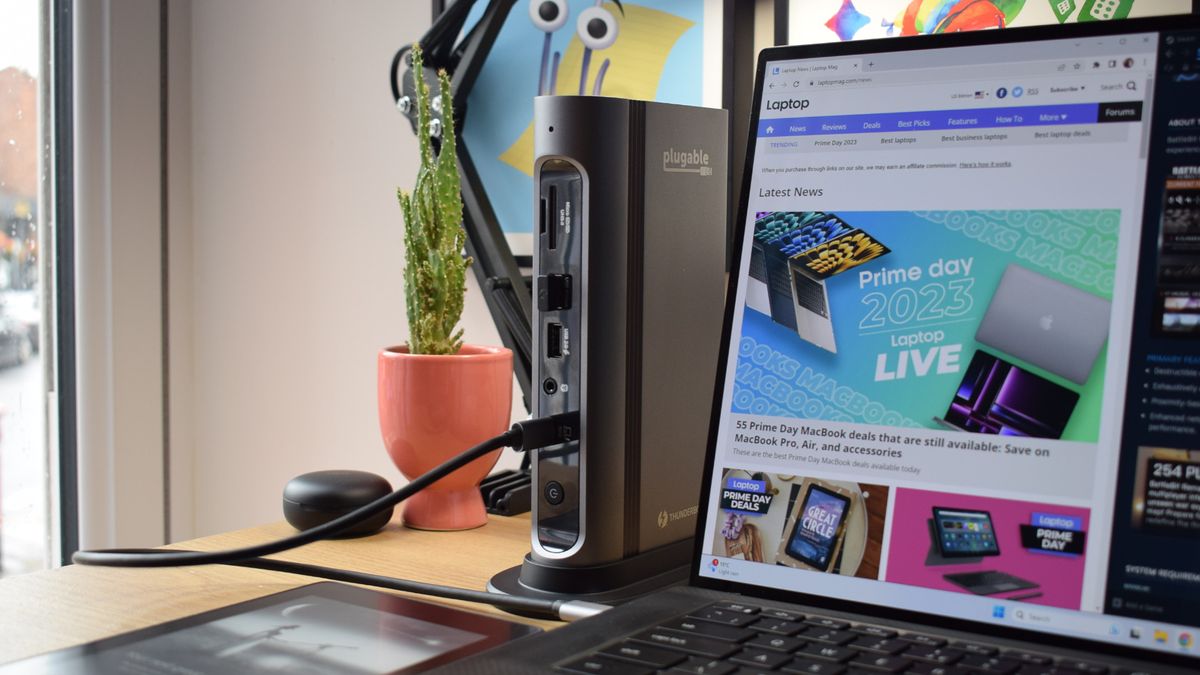 Photo of the Plugable Thunderbolt 4 &amp; USB4 Quad Display Docking Station (TBT4-UDZ) stood vertically with the front-facing Thunderbolt host port connected to a Dell XPS 15 laptop that is showing the Laptop Mag homepage.