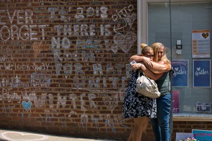 Mourners embrace in front of the hand-written chalk messages that line the walls outside the buildings where one year ago Heather Heyer was killed by a speeding vehicle driven by a white supr