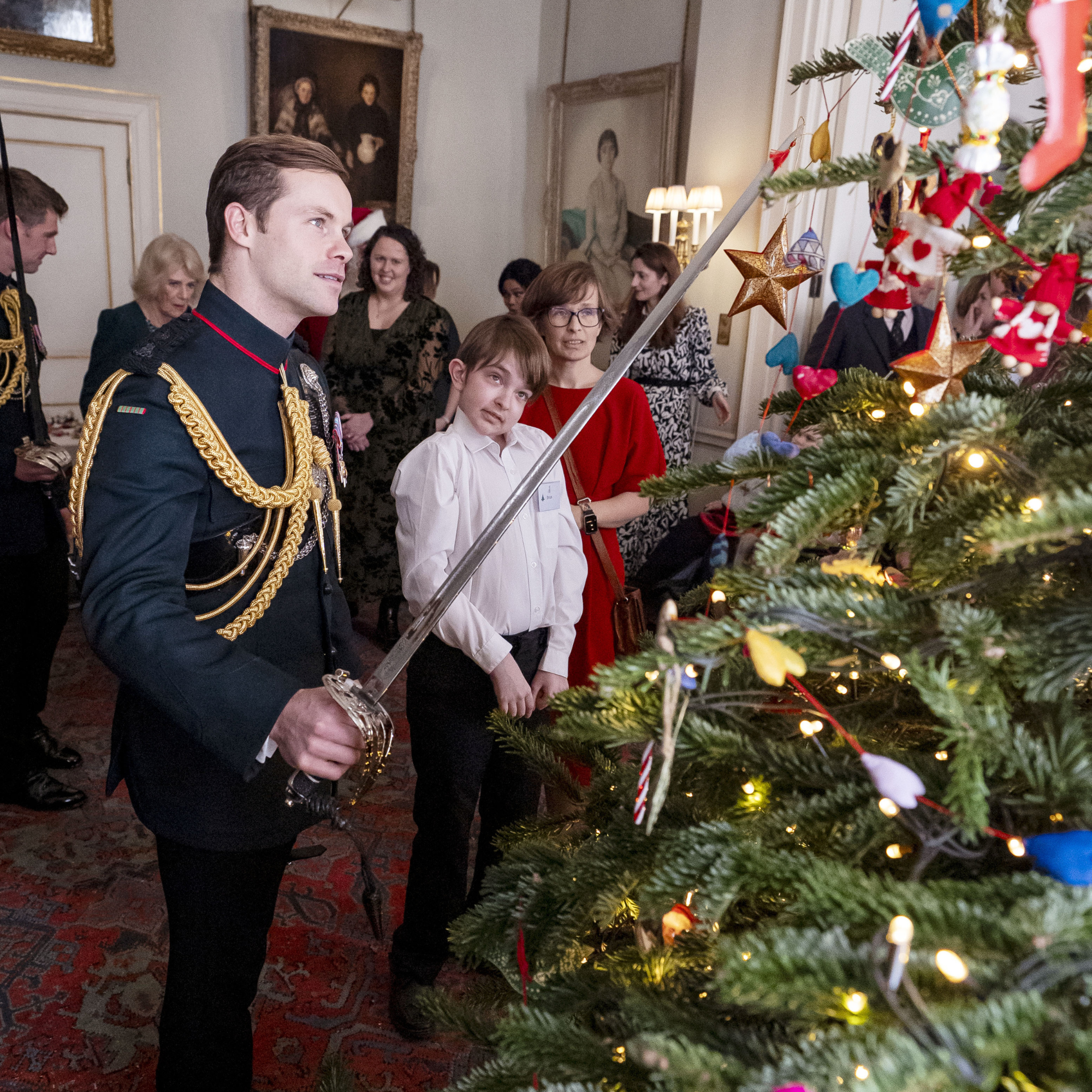 Major Ollie Plunket helps Ivan decorate the Christmas tree using his sword during an event supported by Helen and Douglas House and Roald Dahl's, Marvellous Children's Charity, at Clarence House in London on December 11, 2025 in London, England.