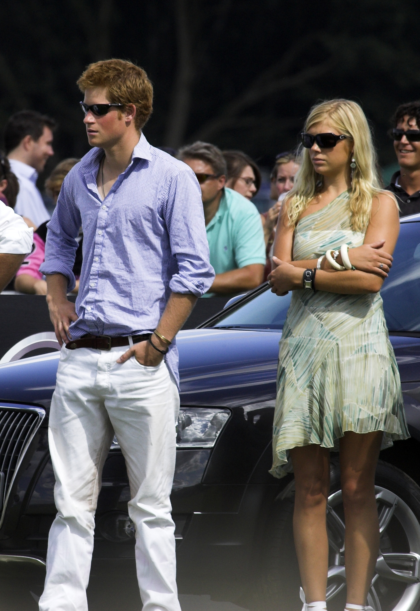 Prince Harry wearing a blue shirt standing next to Chelsy Davy and a car