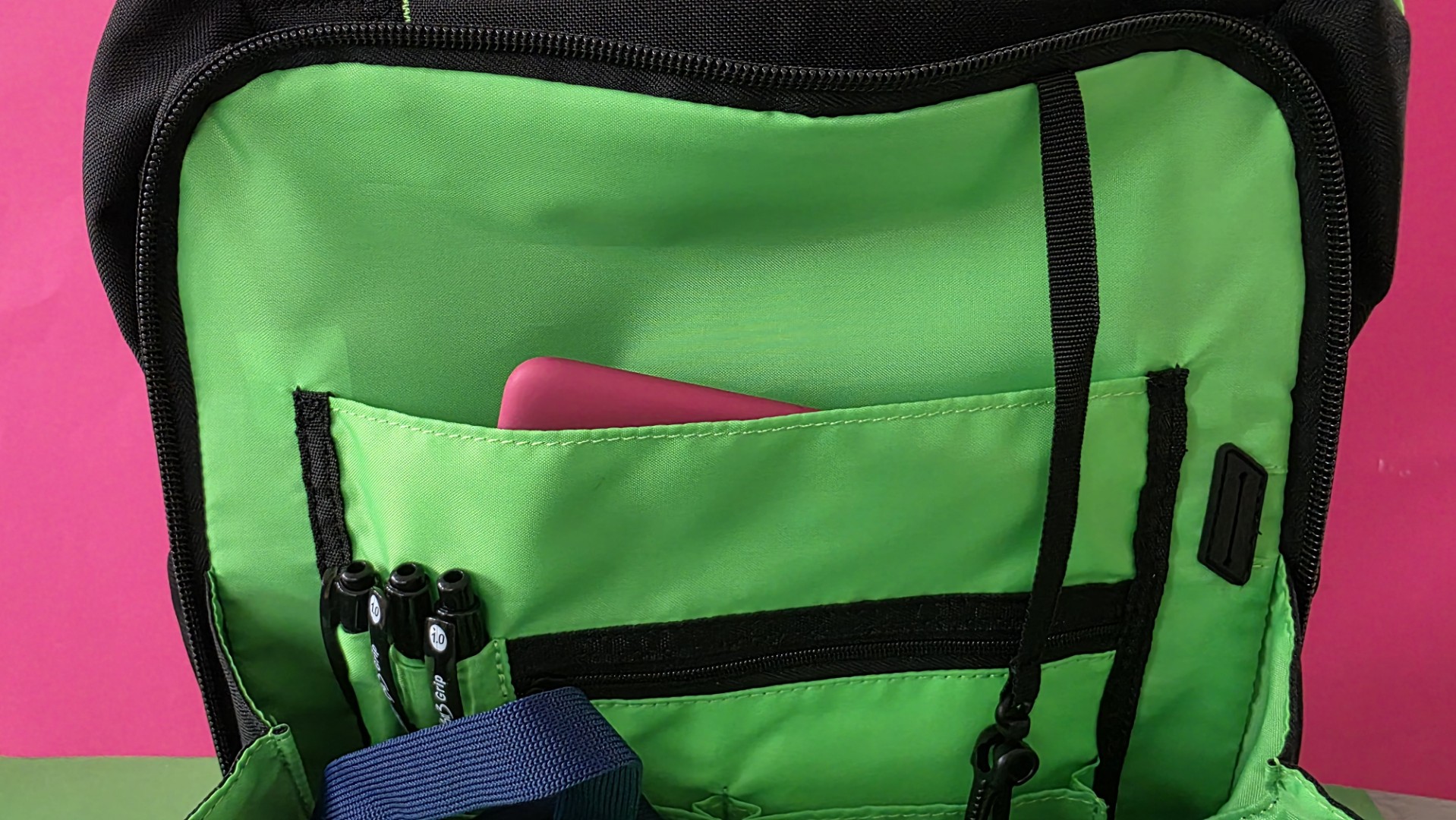 A black Razer backpack front pocket held open, contains pens.