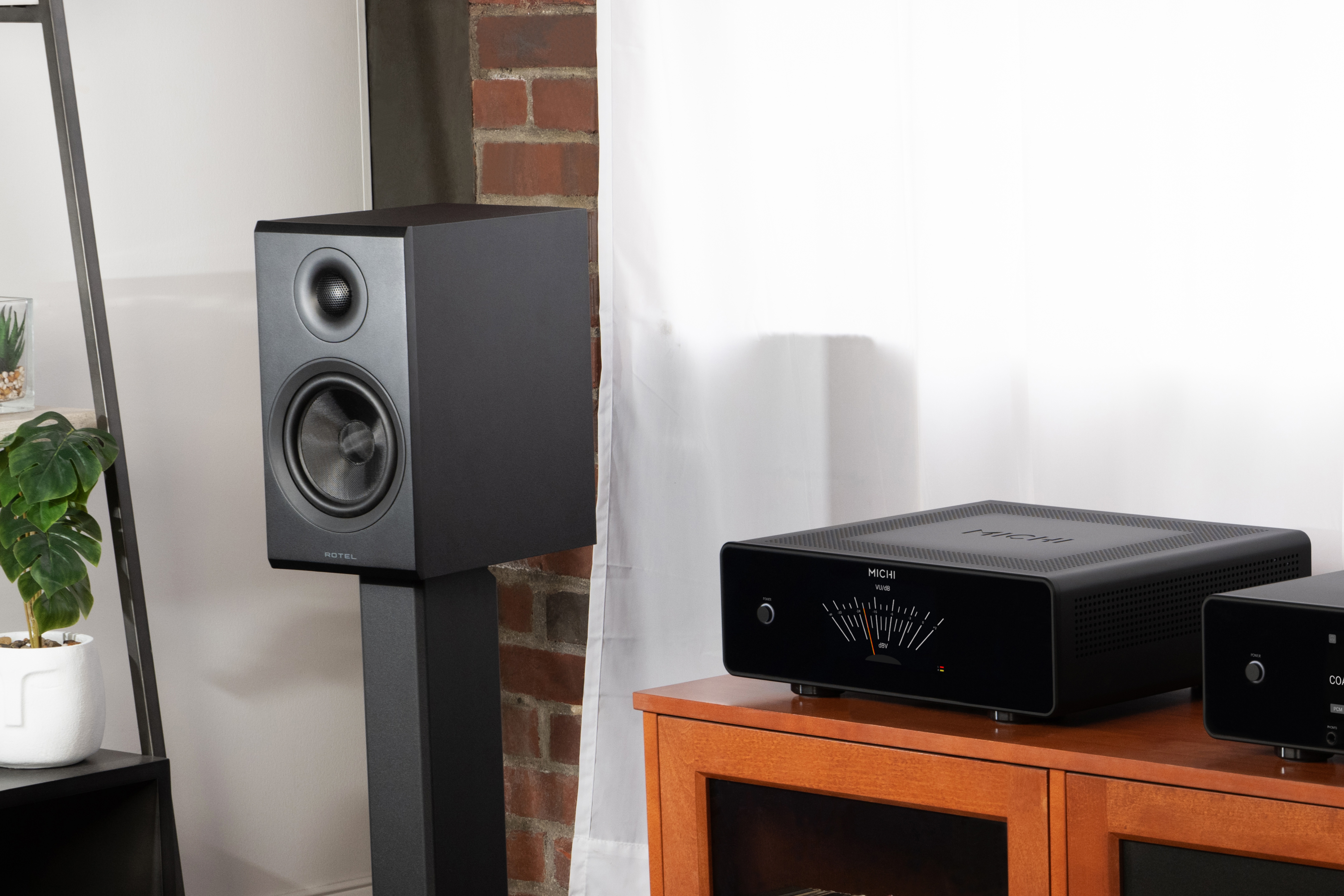 Rotel Amora 5 standmount speakers in black next to a hi-fi system