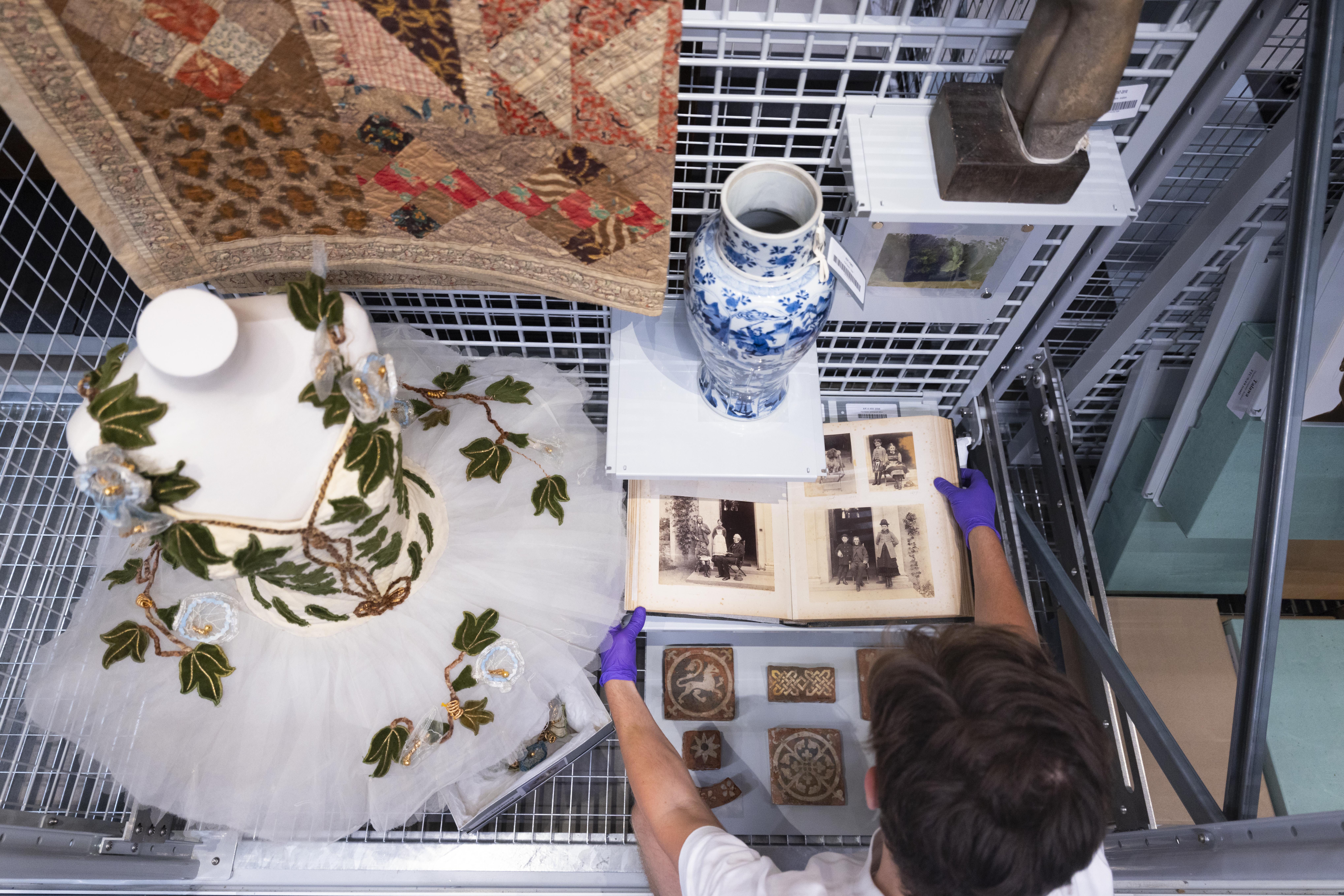 A display of a tutu, quilt, vase and photos and a man's arms arranging them