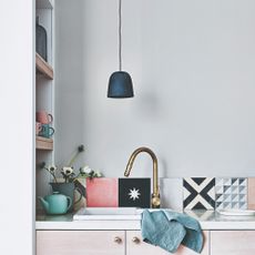 A kitchen with a kitchen sink, a pendant light and backsplash covered in patterned tiles