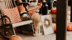 An antique sale with a wooden rocking chair, an orange cushion, and a wooden table surrounded by straw and pumpkins
