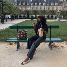 A woman sat on a bench wearing leather trousers