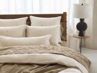 Neutral bedding on a made bed with a black table lamp next to it