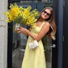 Sara Walker wears a yellow dress, brown sunglasses and a white handbag.