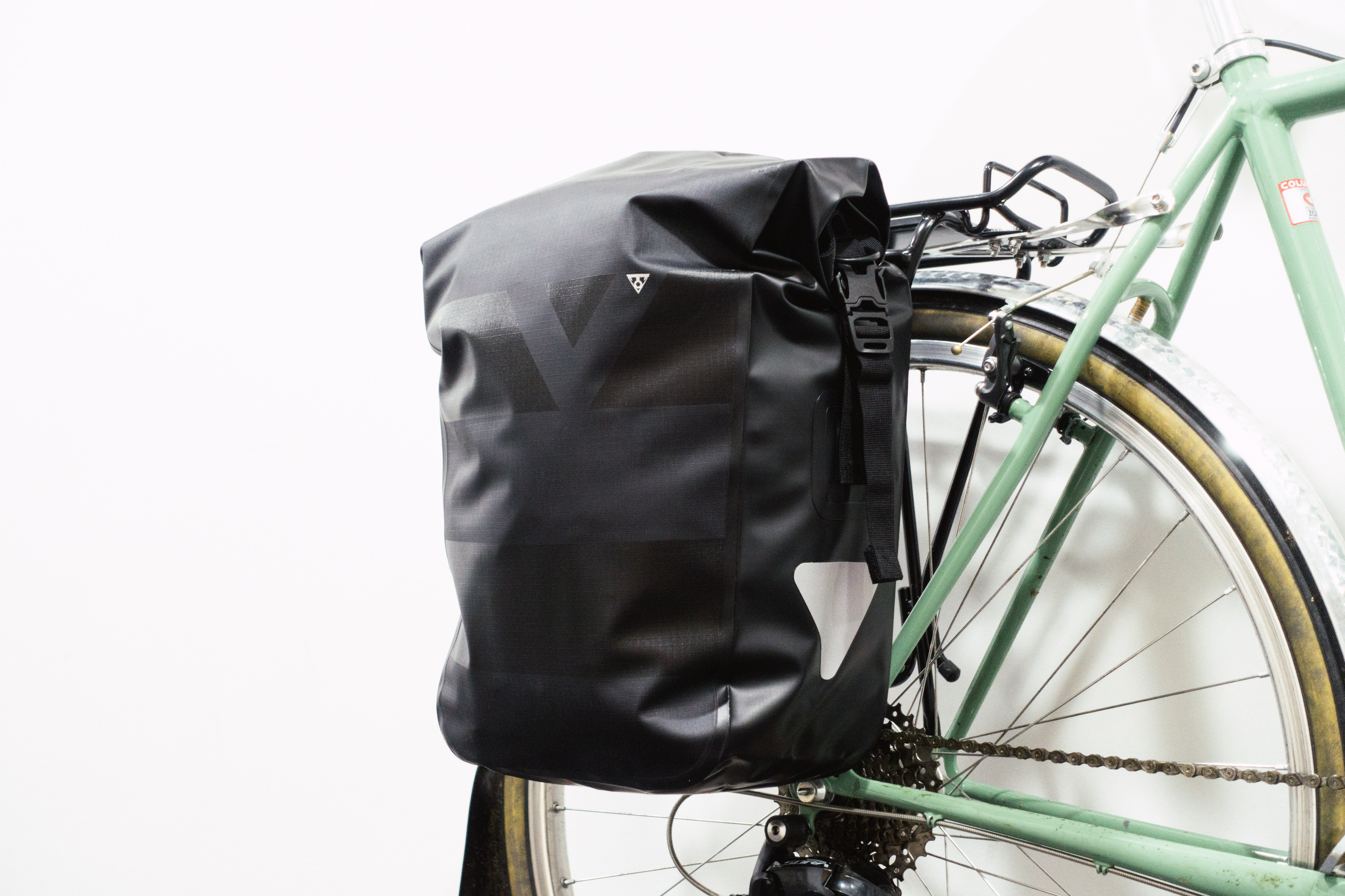 A black pannier mounted to a green bike against a white background