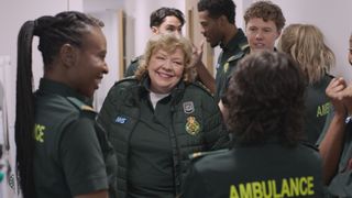 Senior paramedic smiling sarcastically, while surrounded by trainee paramedics checking their exam results.