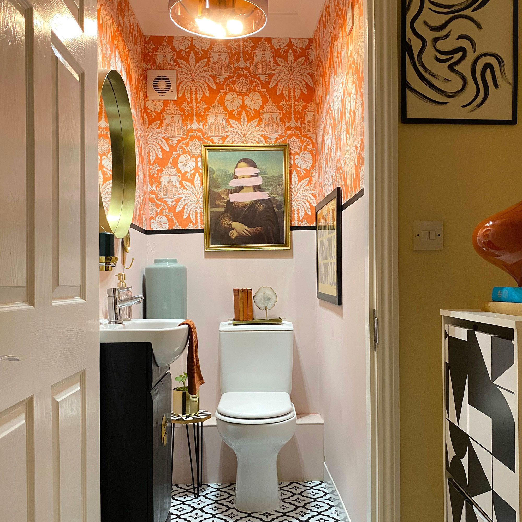 Loo with orange floral wallpaper, artwork and round mirror