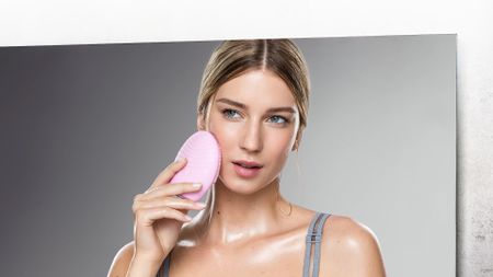 A woman looking in the mirror using the best facial cleansing brush, the Foreo Luna 3