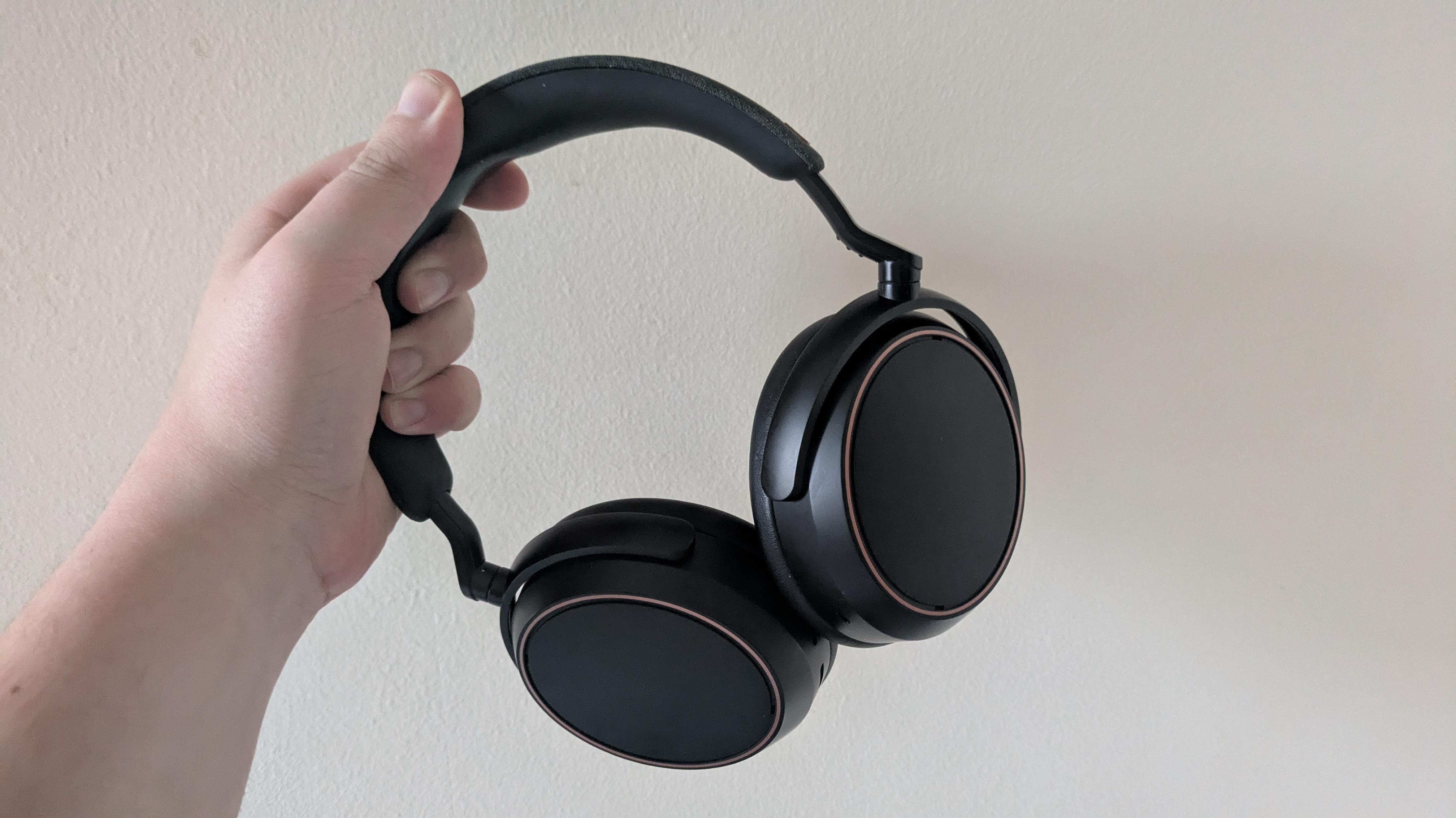 A hand holding a pair of Sennheiser Momentum 4 Wireless headphones against a wall 