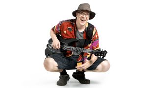 Devin Townsend squatting in a hat and colourful shirt