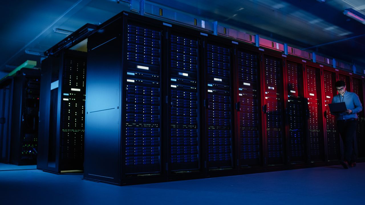 IT Specialist Walks along the Row of Operational Server Racks in a data centre, Uses Laptop for Maintenance