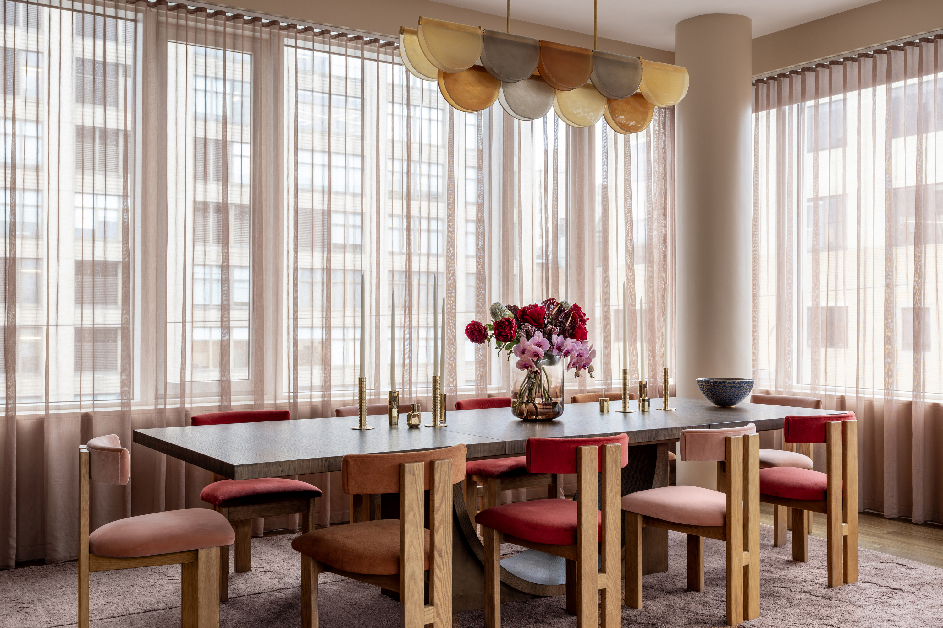 A dining room with 10-seater, pink-toned chairs and a multicolored light 
