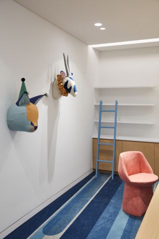 An office room with striped blue carpet, a pink chair and textile animal heads on the walls
