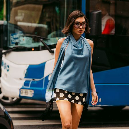 Woman wears silky blue halter top and polka dot mini skirt while walking on a cross walk. 