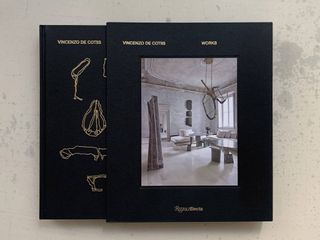 The black cover of a book features organically drawn sketches of objects in gold and a photograph of a superbly, modern designed living room.