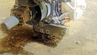 A large machine digs into reddish dirt with a drill