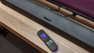 A Roku remote and sound bar in front of a TV