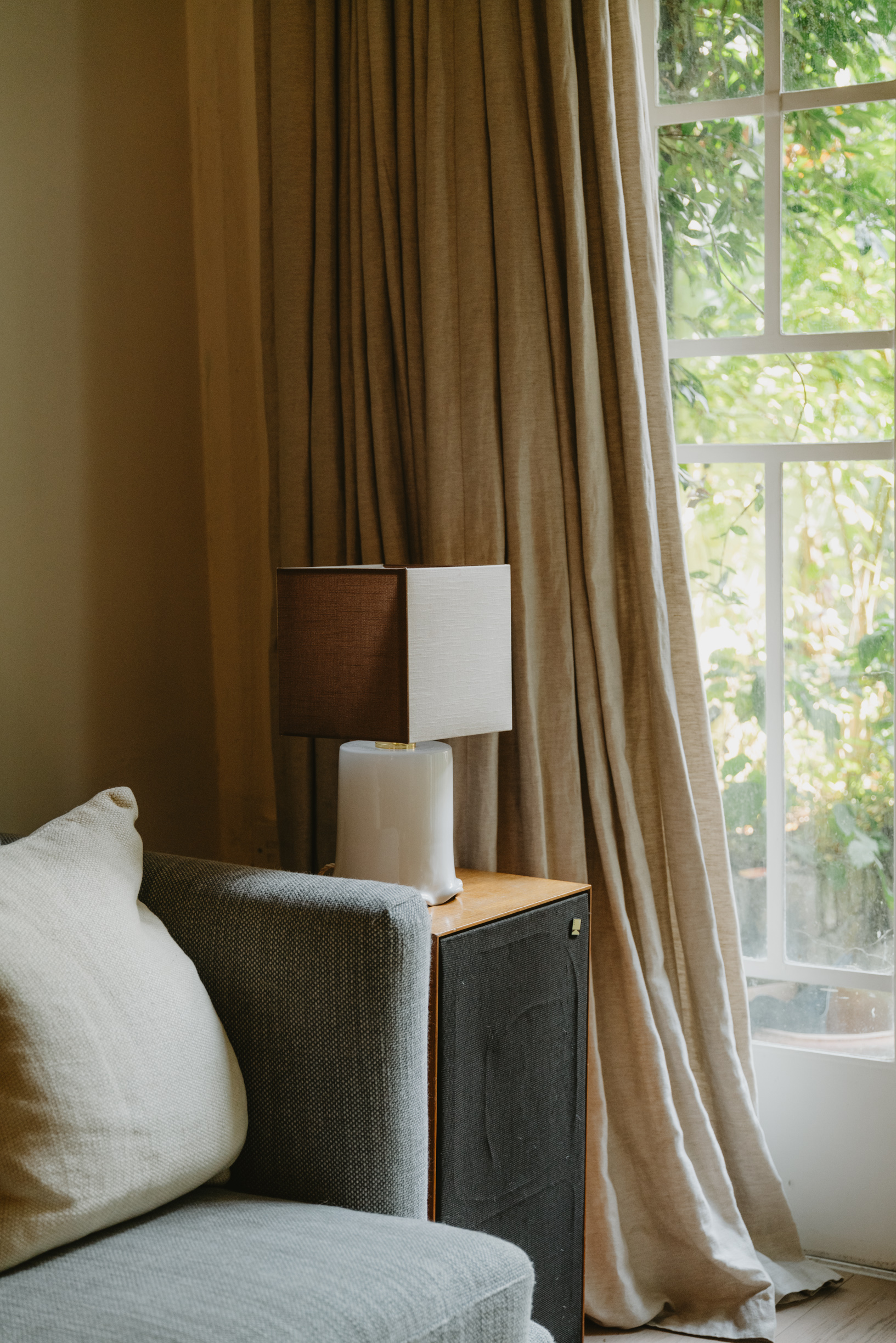 Image of a white and brown lamp on a side table in the corner of a beige living room.