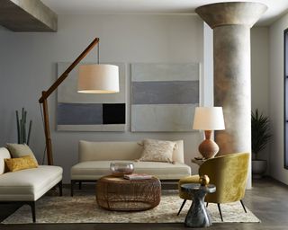 Large wooden floor and table lamps illustrate how to plan living room lighting in a neutral color scheme with large concrete pillar.