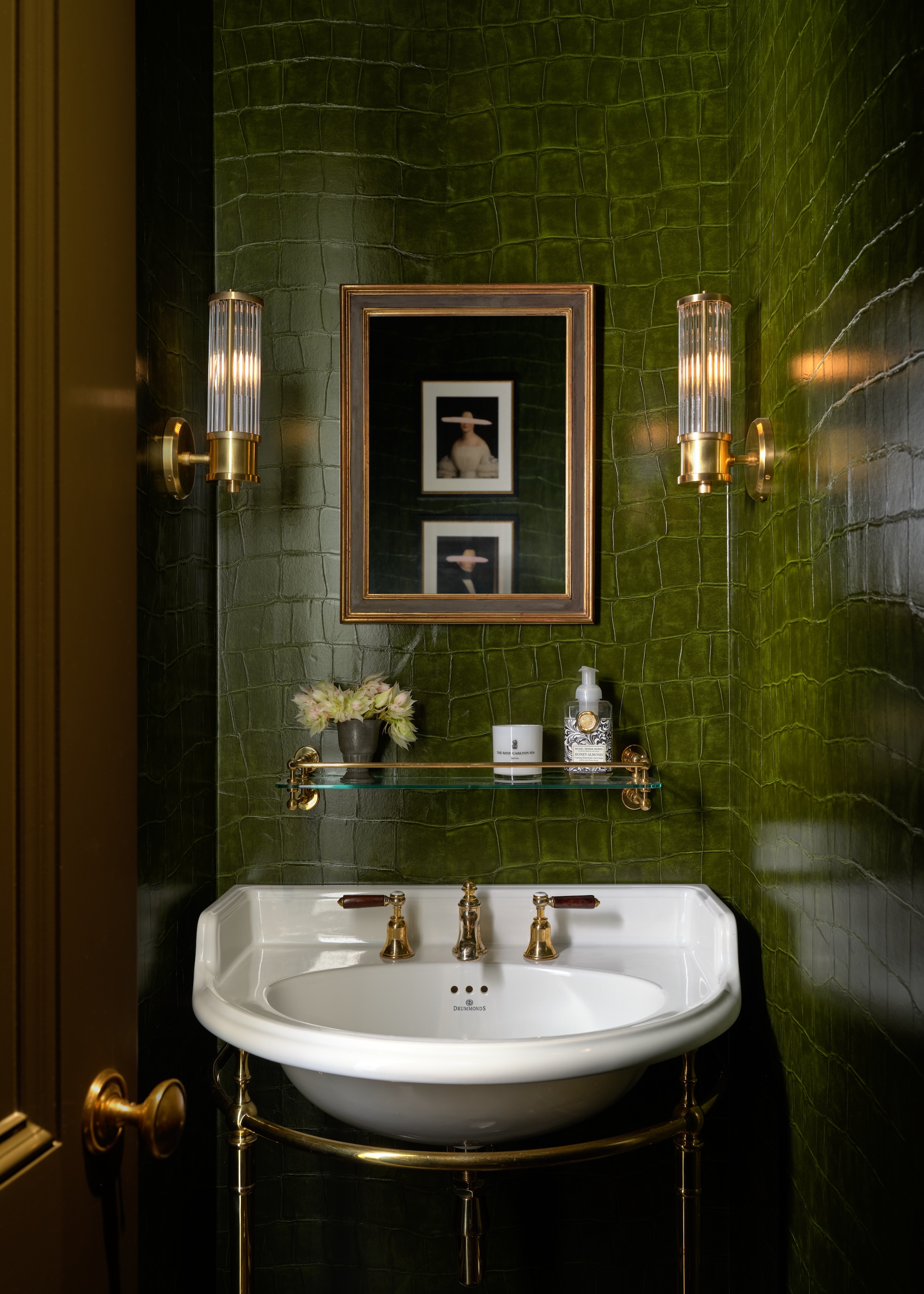 a luxuriously dark green cloakroom shown with croc effect vinyl wallpaper, a classic basin on brass stand and brass wall lights