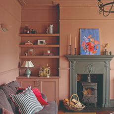 A colour-drenched living room in Farrow & Ball's Sulking Room Pink with a grey sofa and a contrasting dark green fireplace 