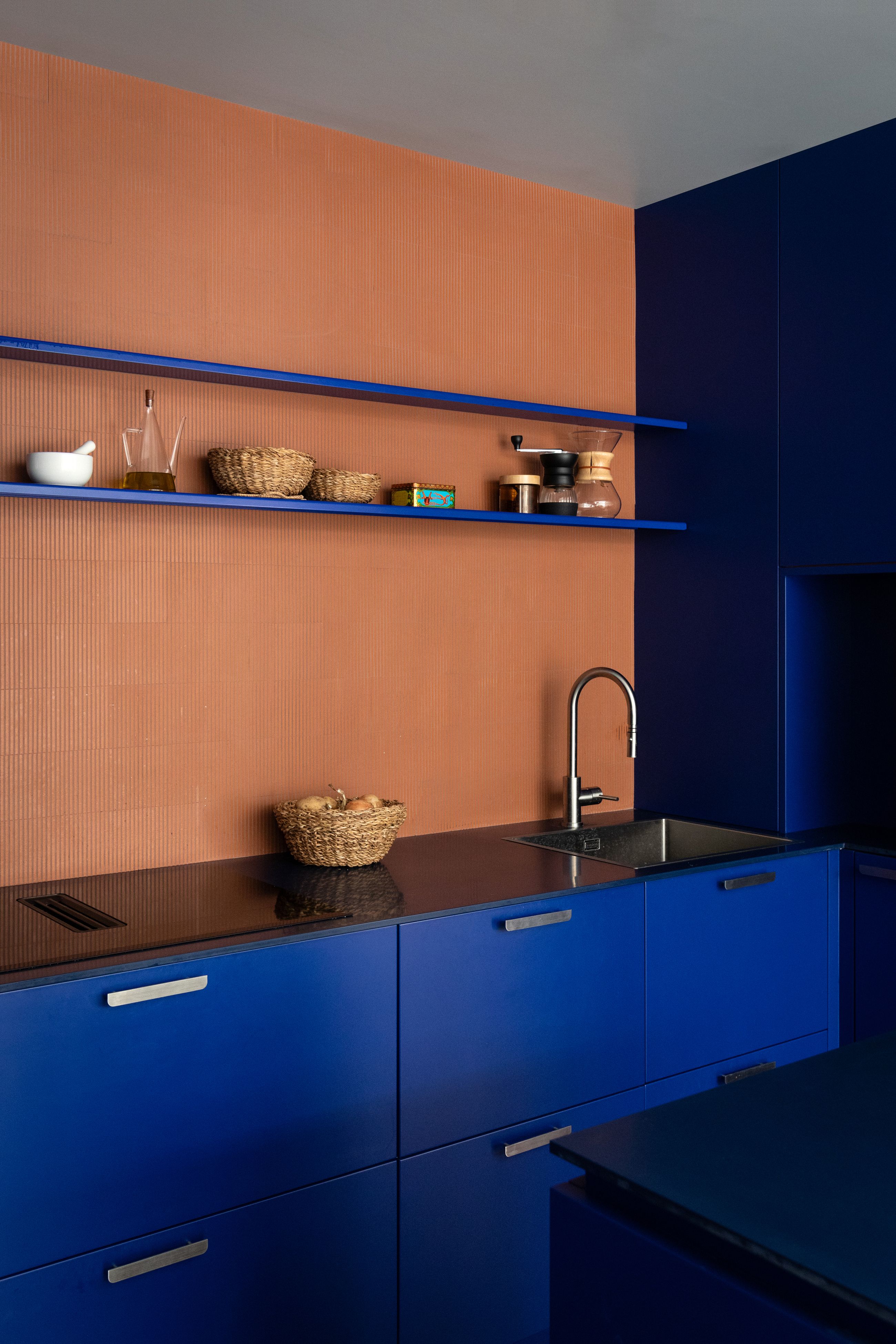 Two kitchens with orange walls, and electric blue cabints, island and shelves