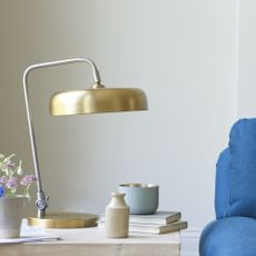 Biblio Table Lamp in Brass on a side table next to a blue couch