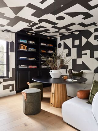 Home office space with bold black-and-white geometric wallpaper and a white corner couch with a black table and black bookcase