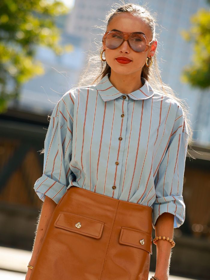 A woman at London Fashion Week wearing a blue striped shirt, sunglasses and a bold red lip