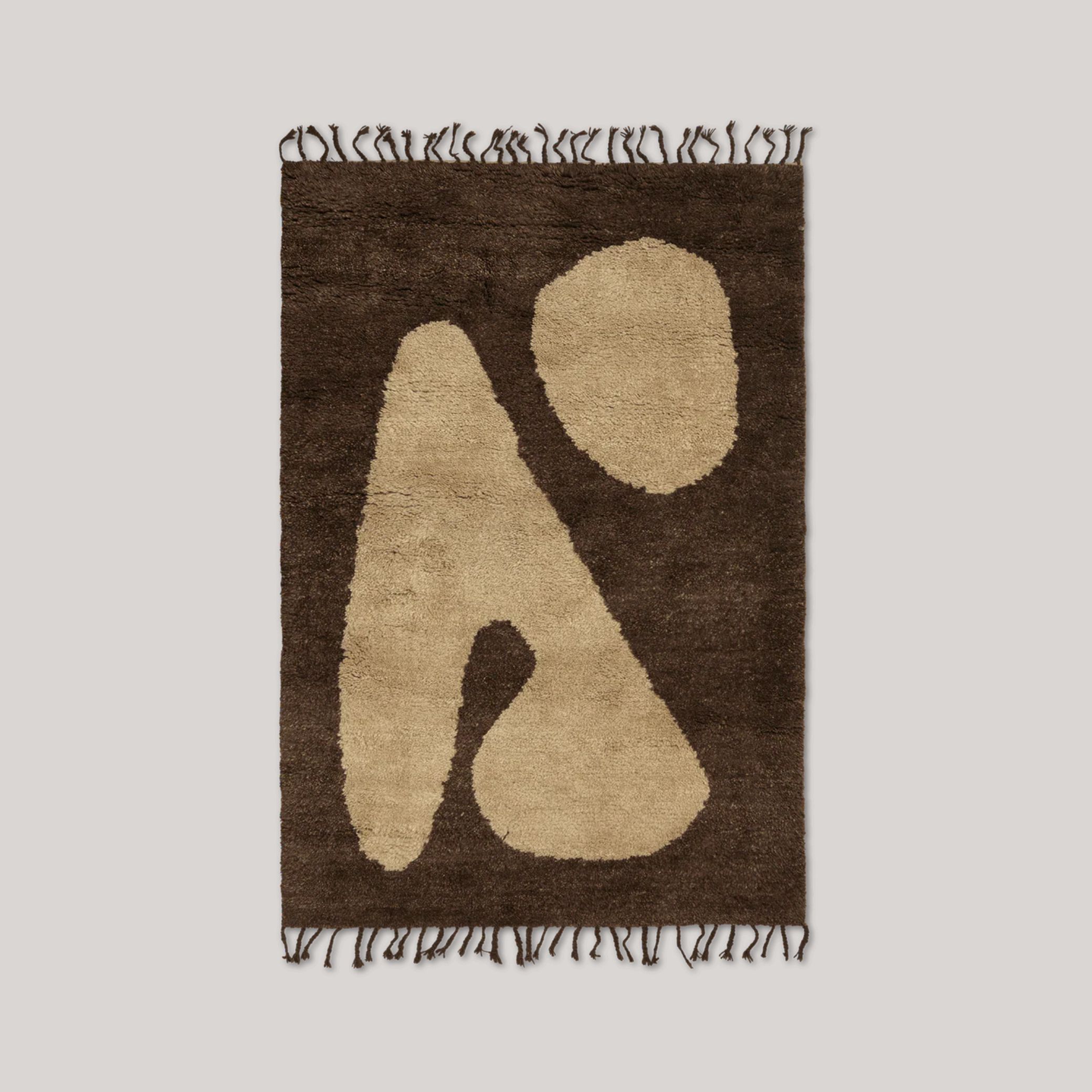 An abstractly decorated rug in brown and off white shows a vague human silhouette and is shown against a pale gray background.