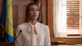 Chloe in the witness stand in court looking worried and wearing a silky pale pink blouse